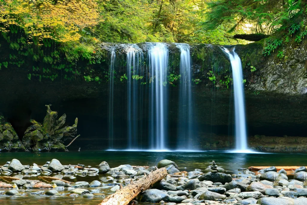 The benefits of spending time in nature include being present in the moment. This image depicts a waterfall cascading into a natural pool, with lush green forest in the background. The sight and sound of the water both create a sense of serenity.