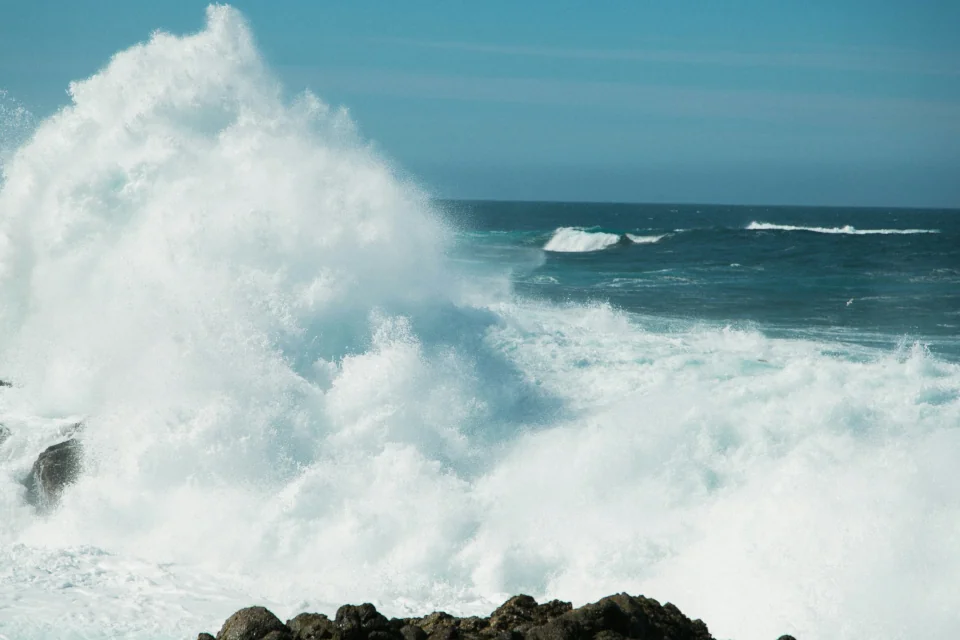A wave breaking on the rocky shore spaying water high into the air.