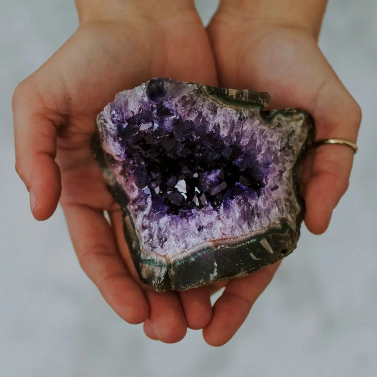 Two hands cupped holding a amethyst cluster.