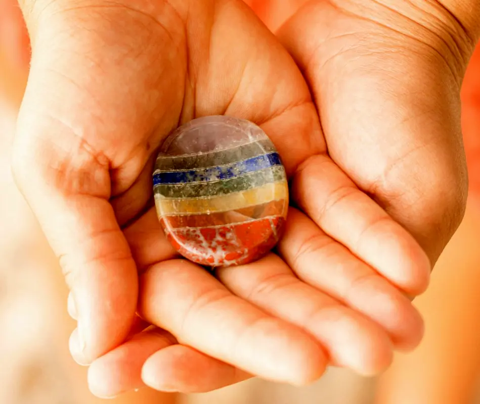 Two hands holding a multi colour stone.